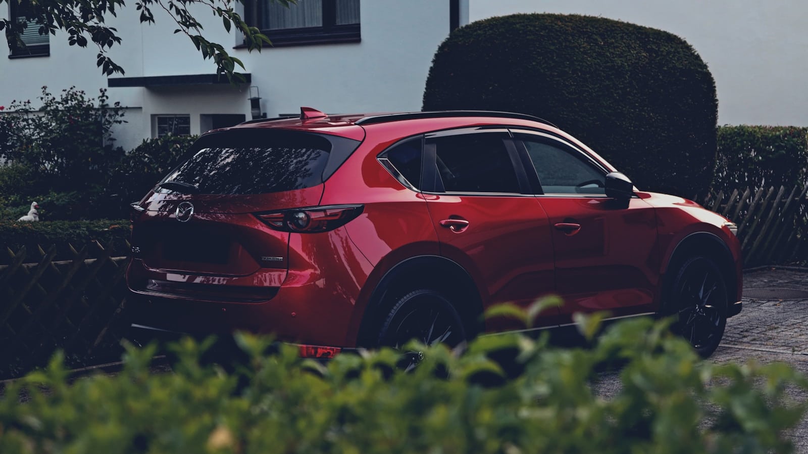a red car parked in front of a hedge
