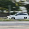 A white car driving down a street next to a forest