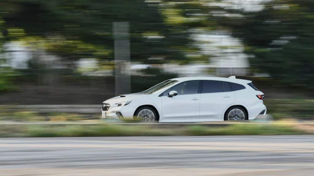 A white car driving down a street next to a forest